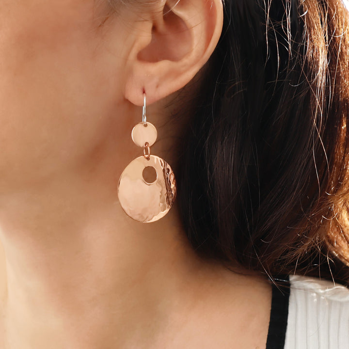 Close-up of a woman wearing two tone 925 silver and hammered copper dangling circle disc earrings with a blurred background