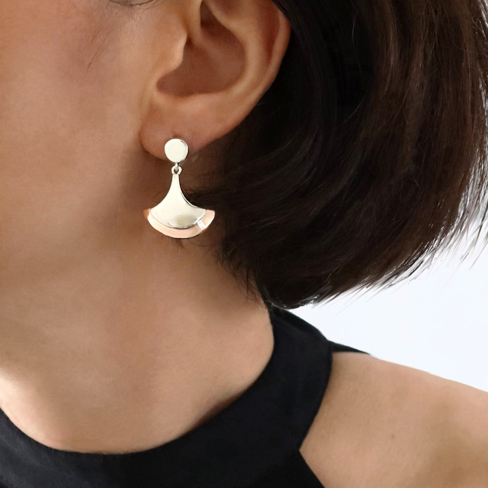 A woman wearing a pair of two-tone copper earrings with sterling silver accents, in a fan-shaped design.