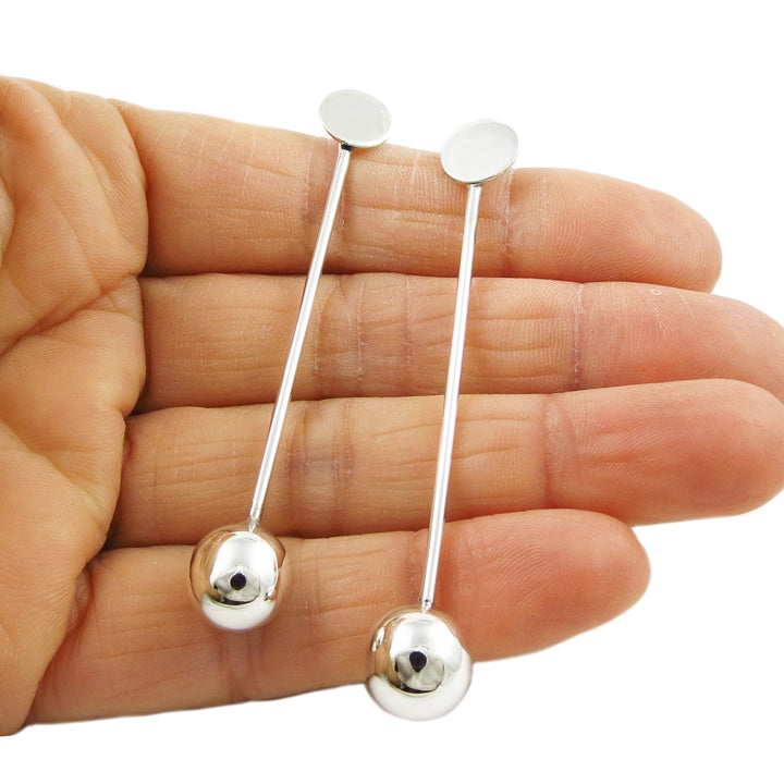 Long 925 silver earrings held between fingers on a white background