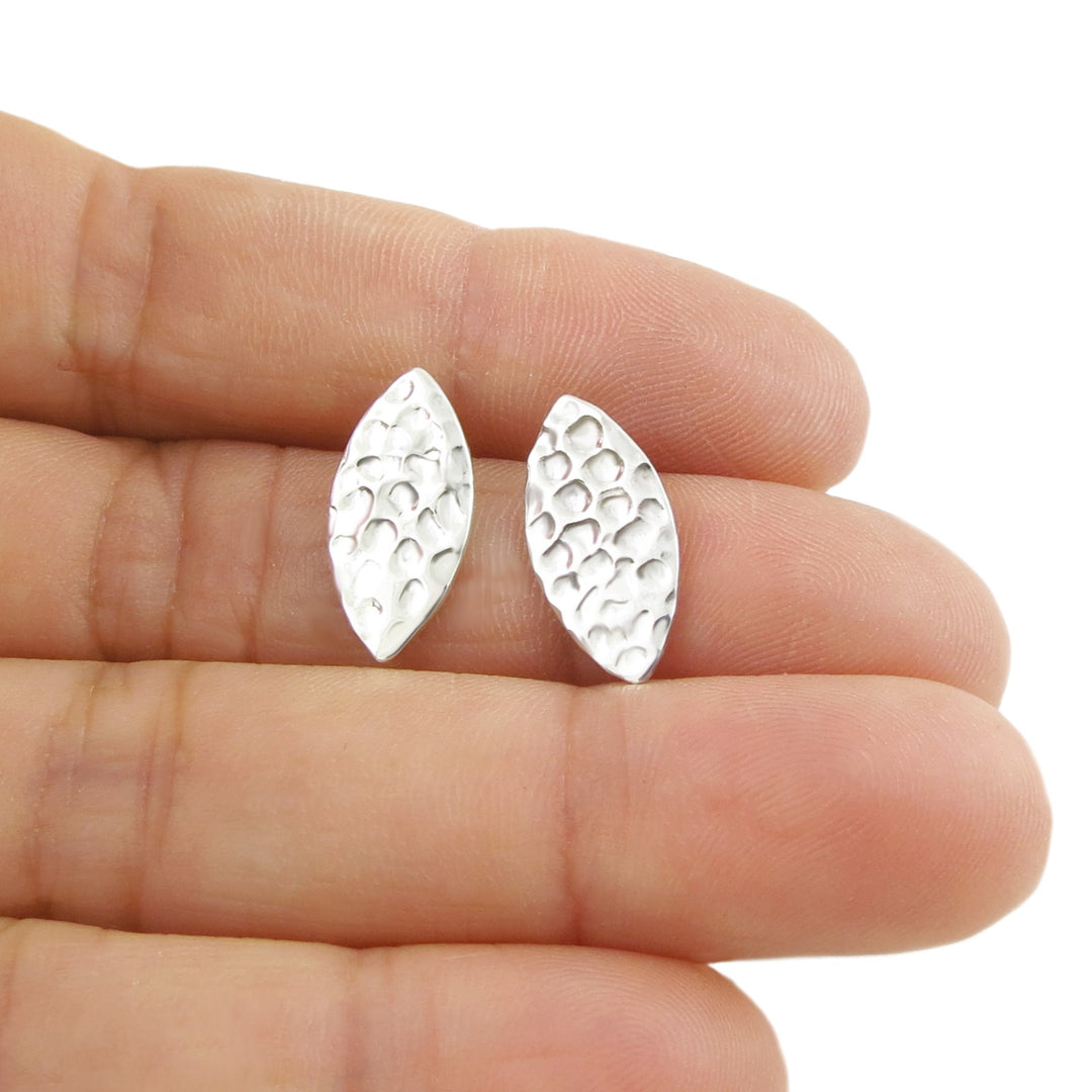 925 silver elliptical shaped stud earrings with a hammered finish held in a persons hand.