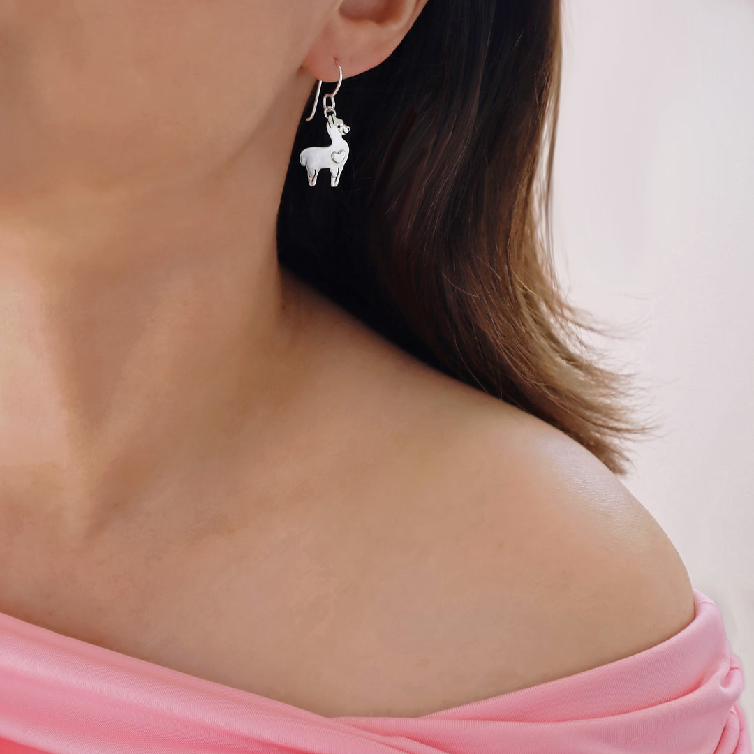A close-up of a model wearing a unique Mexican 925 silver llama dangle earring, with her shoulder and hair visible against a soft light background.
