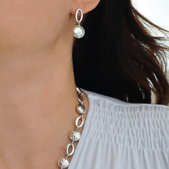 Close-up of a woman wearing silver dangling earrings with a blurred background