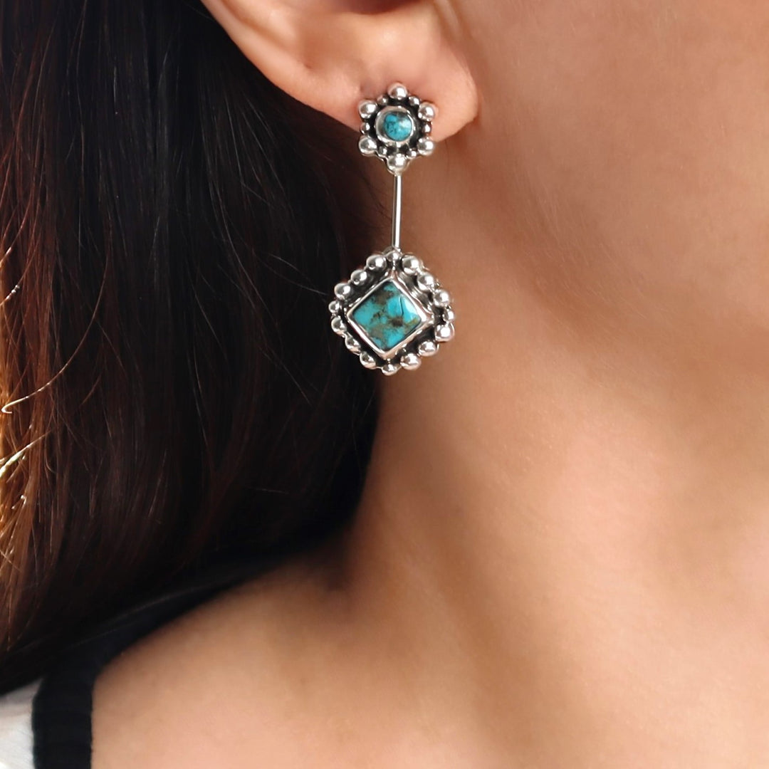 Close-up of a person wearing a silver earring with turquoise stones.