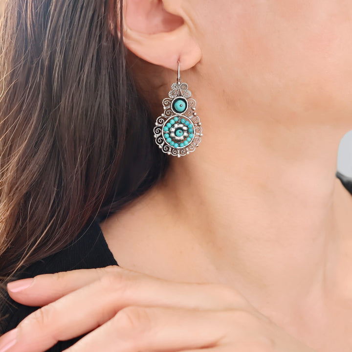 Ornate turquoise filiree earrings being worn by a person with a black blouse