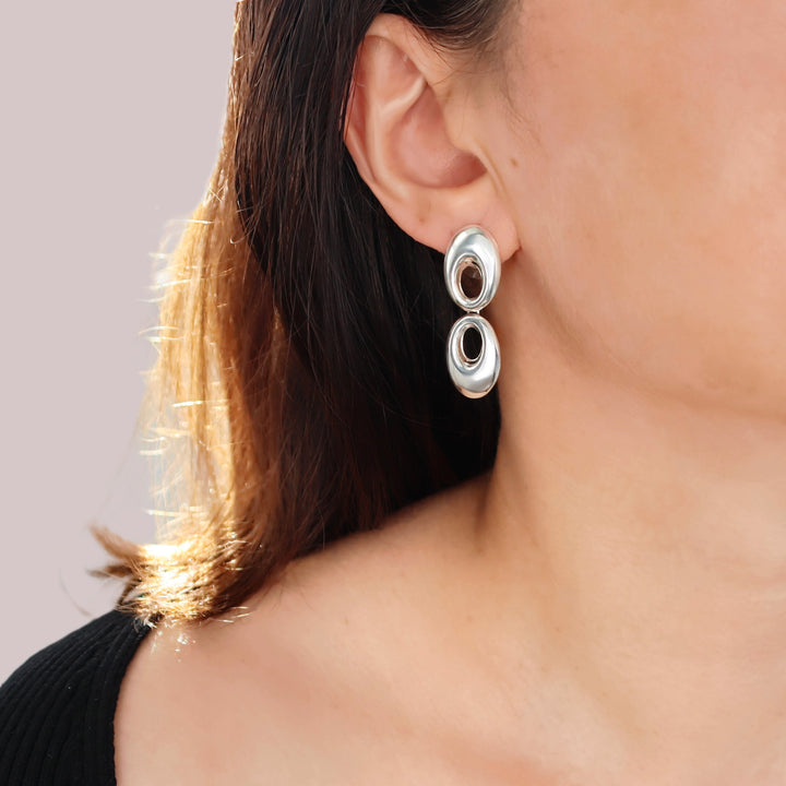 Close-up of a person wearing silver hoop earrings with a neutral background