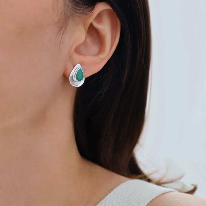 Teardrop-shaped silver and green gemstone earring worn by a person with a neutral background