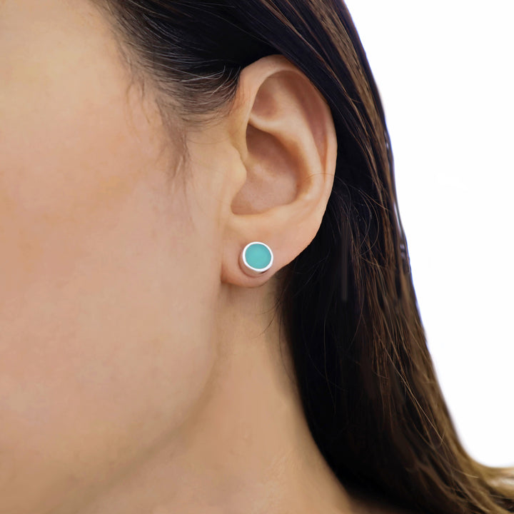 Close-up of an ear wearing a green gemstone stud earring on a white background