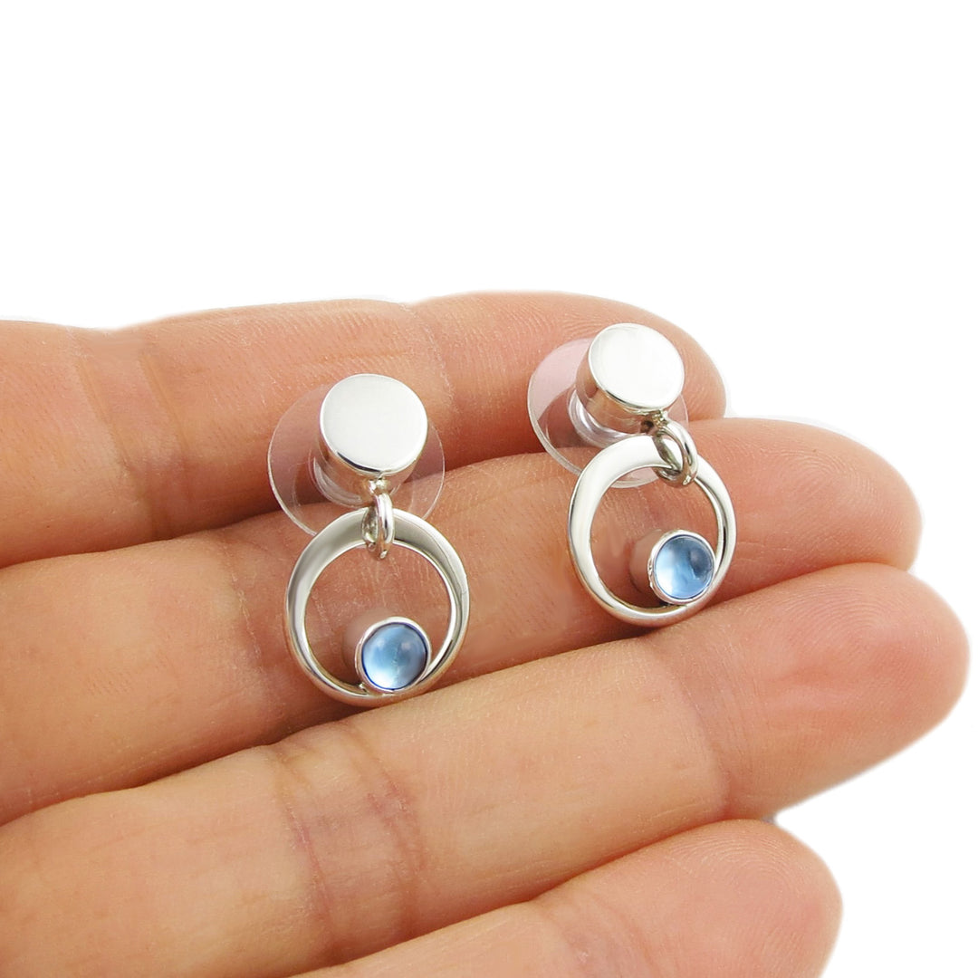 Silver earrings with blue topaz stones held between fingers on a white background