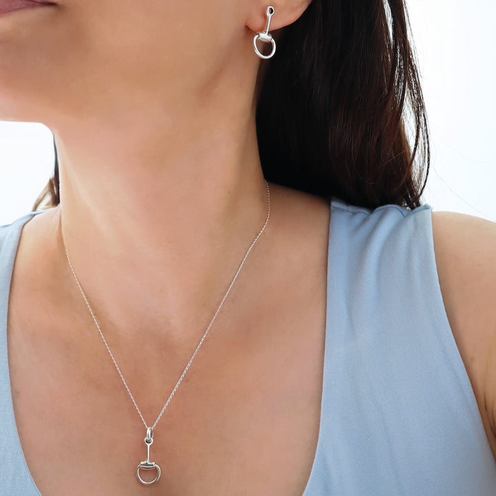 Silver equestrian-themed necklace and earrings on a person wearing a light blue top.