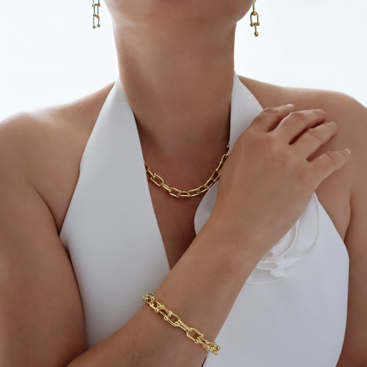 Gold gauge link chain earrings, necklace and bracelet worn by a woman with a white waistcoat. 