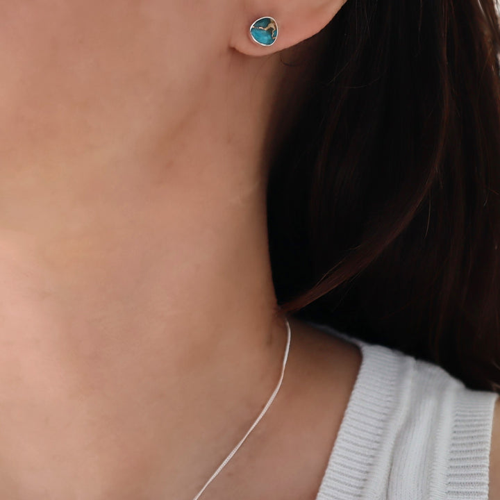 Close-up of a person wearing turquoise earrings with a neutral background