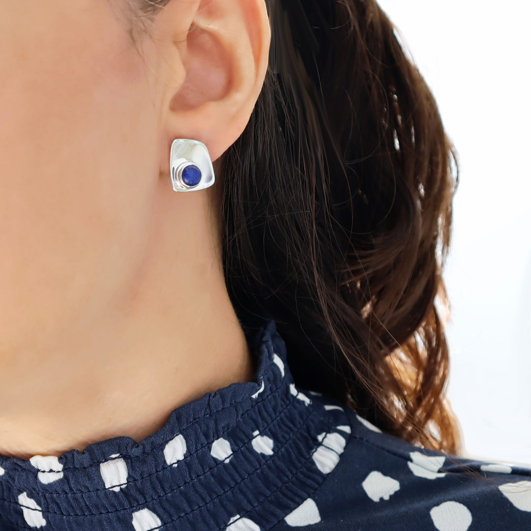 Close-up of a woman wearing silver earrings with a blue lapis lazuli gemstone on a white background