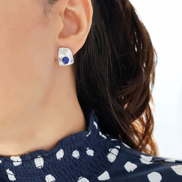 Close-up of a woman wearing silver earrings with a blue lapis lazuli gemstone on a white background