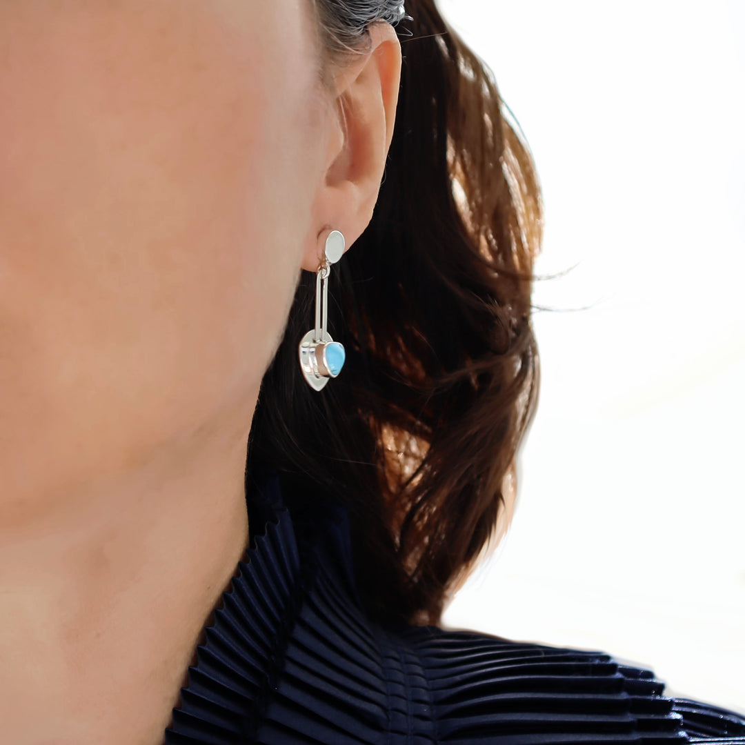 A woman in a blue silk blouse wearing a silver earring with a natural turquoise gemstone. 