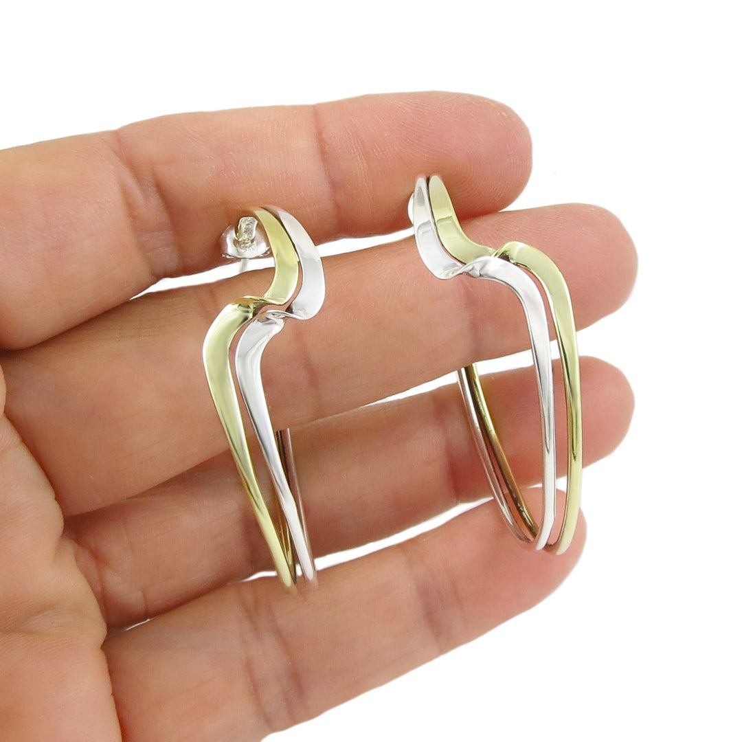 Gold and silver earrings held between fingers on a white background