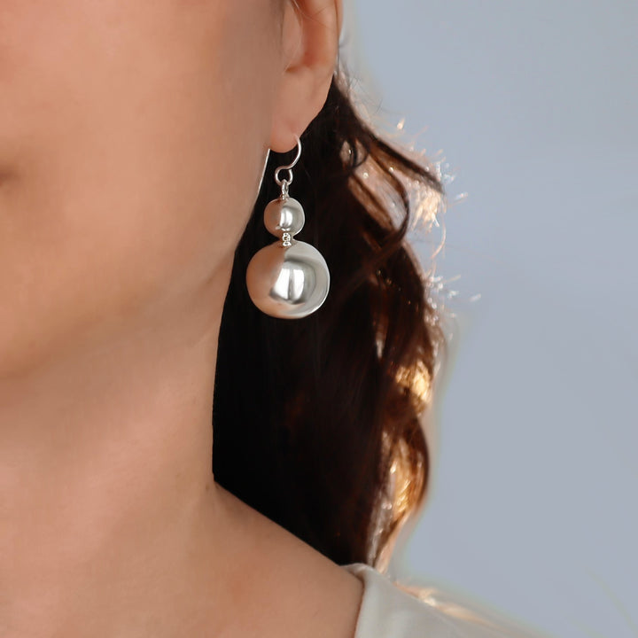 A woman with dark hair wearing  a large over-sized double all bead drop earring in 925 sterling silver with a polished finish. 