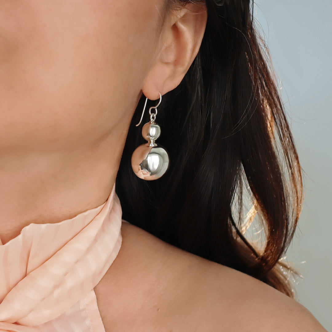Close-up of a woman wearing a large 925 sterling silver double ball bead dangling drop earrings with a neutral background