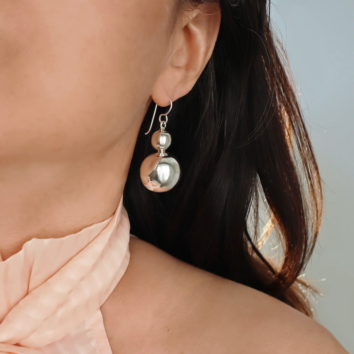 Close-up of a woman wearing a large 925 sterling silver double ball bead dangling drop earrings with a neutral background