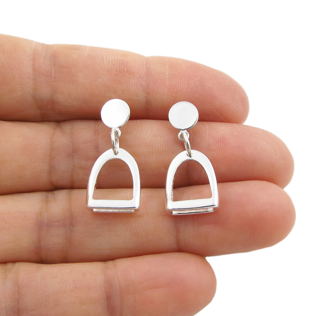 A pair of 925 silver drop earrings with round studs and arch-shaped horse stirrup dangling drops, shown resting on a person's fingers against a white background.