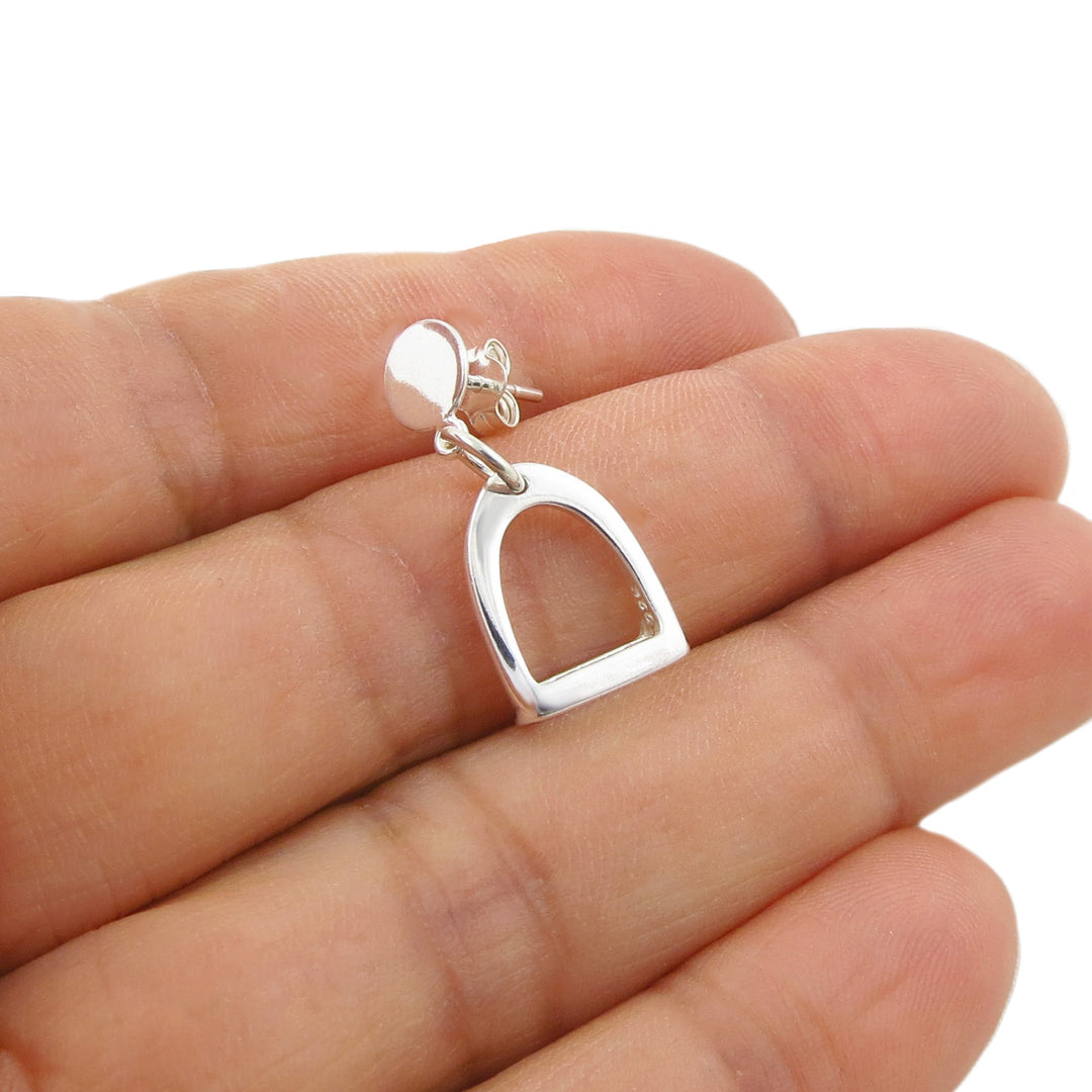 A polished sterling 925 silver equestrian horse stirrup single earring held in a person's hand against a white background.
