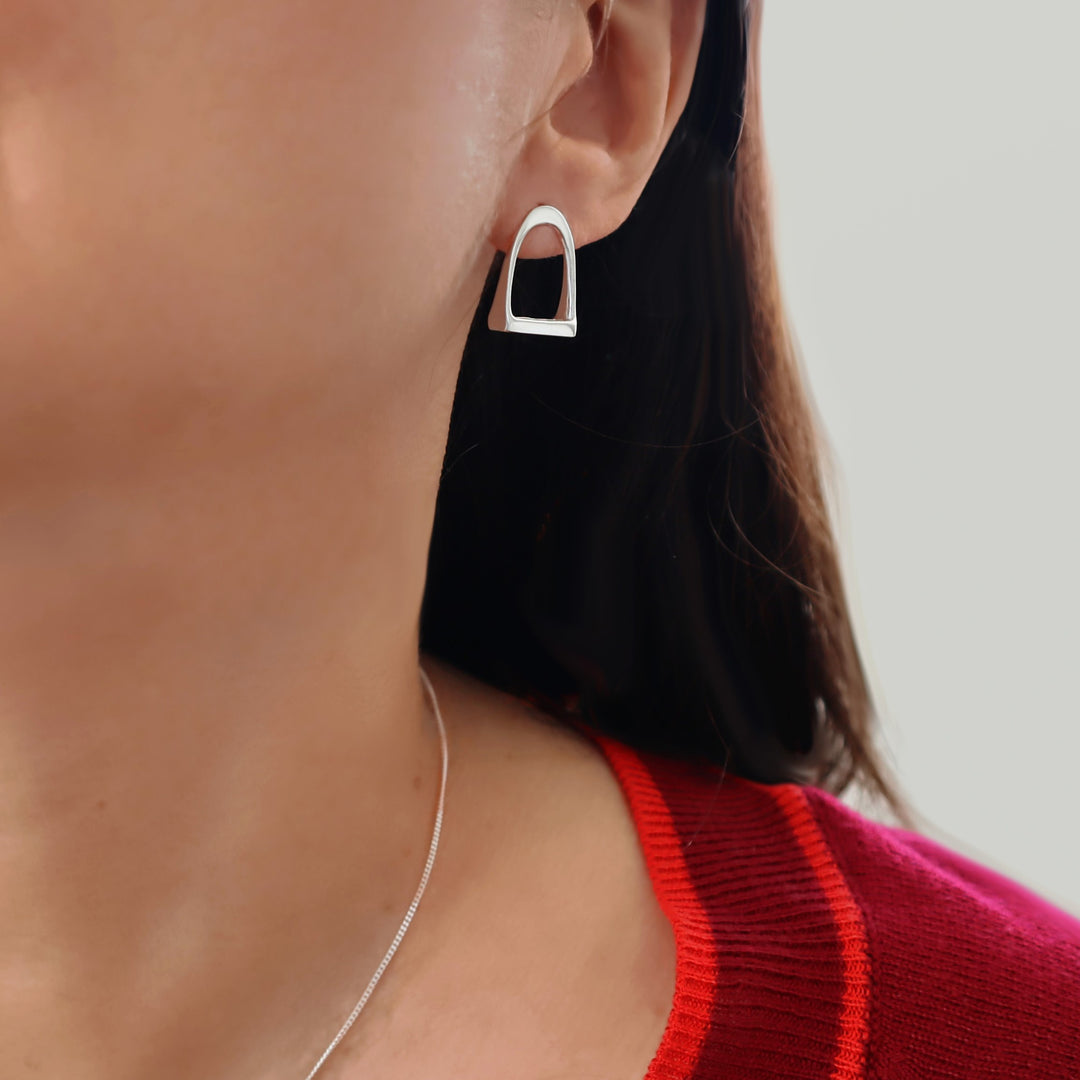 Close-up of a woman wearing a large horse stirrup earrings in quality 925 sterling silver with a red jumper visible