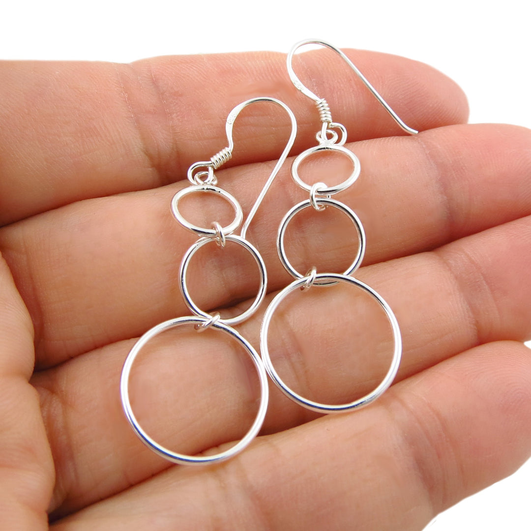 Sterling 925 silver triple hoop dangling earrings held in a hand against a white background