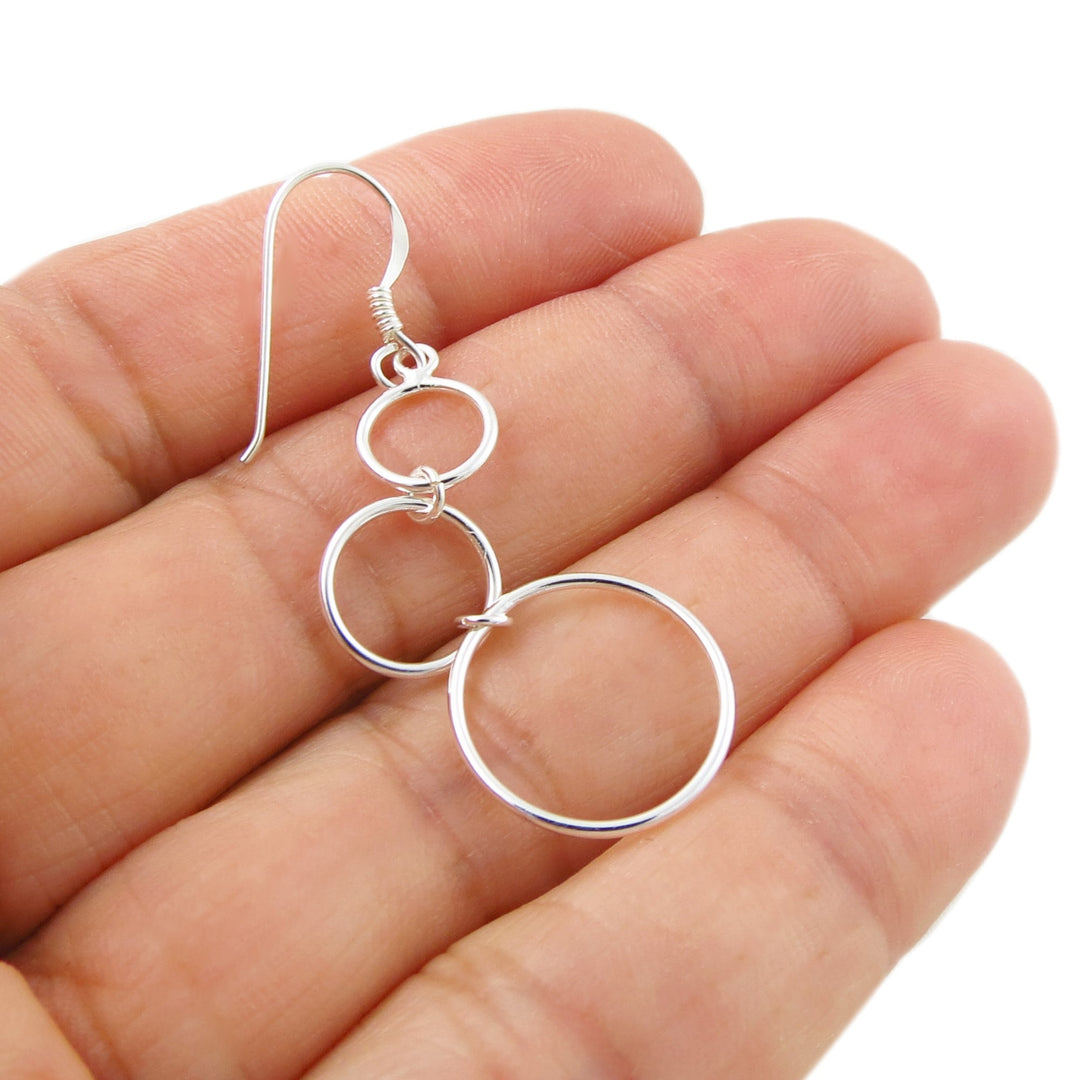 A single 925 sterling silver circle hoop earring held between a woman's fingers on a white background