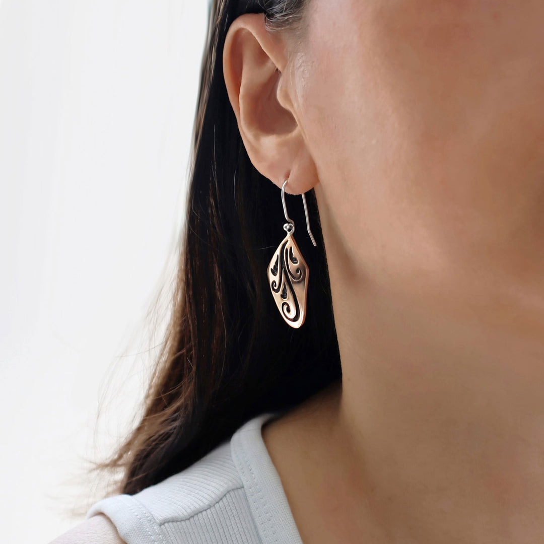 Close-up of a woman wearing a silver and copper mixed metal earring with intricate design.