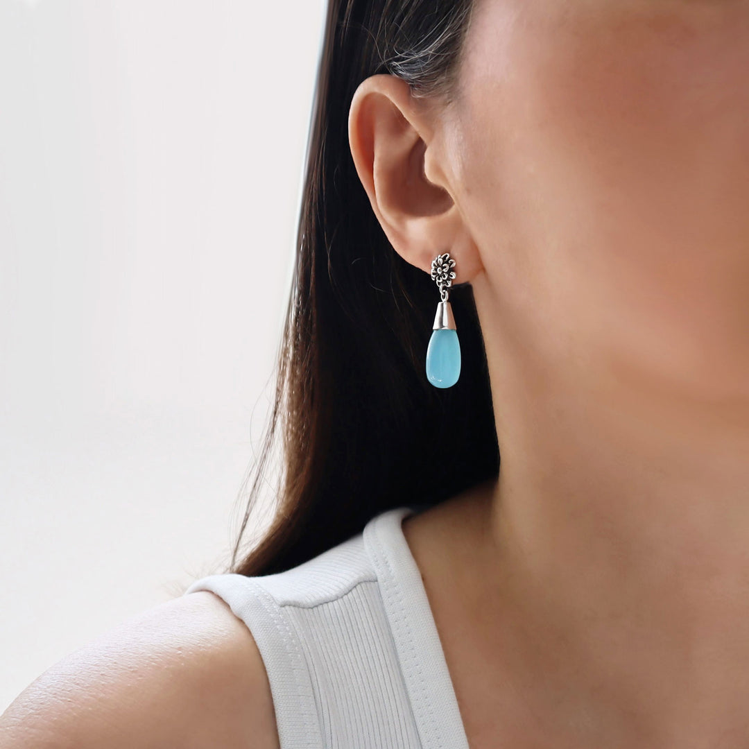 Close-up of a woman wearing a turquoise blue chalcedony and sterling 925 silver teardrop earring with a blurred background