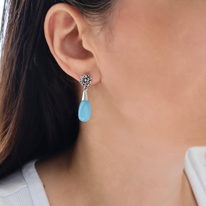 Close-up of a woman wearing a blue chalcedony gemstone teardrop earring with a 925 silver flower accent.