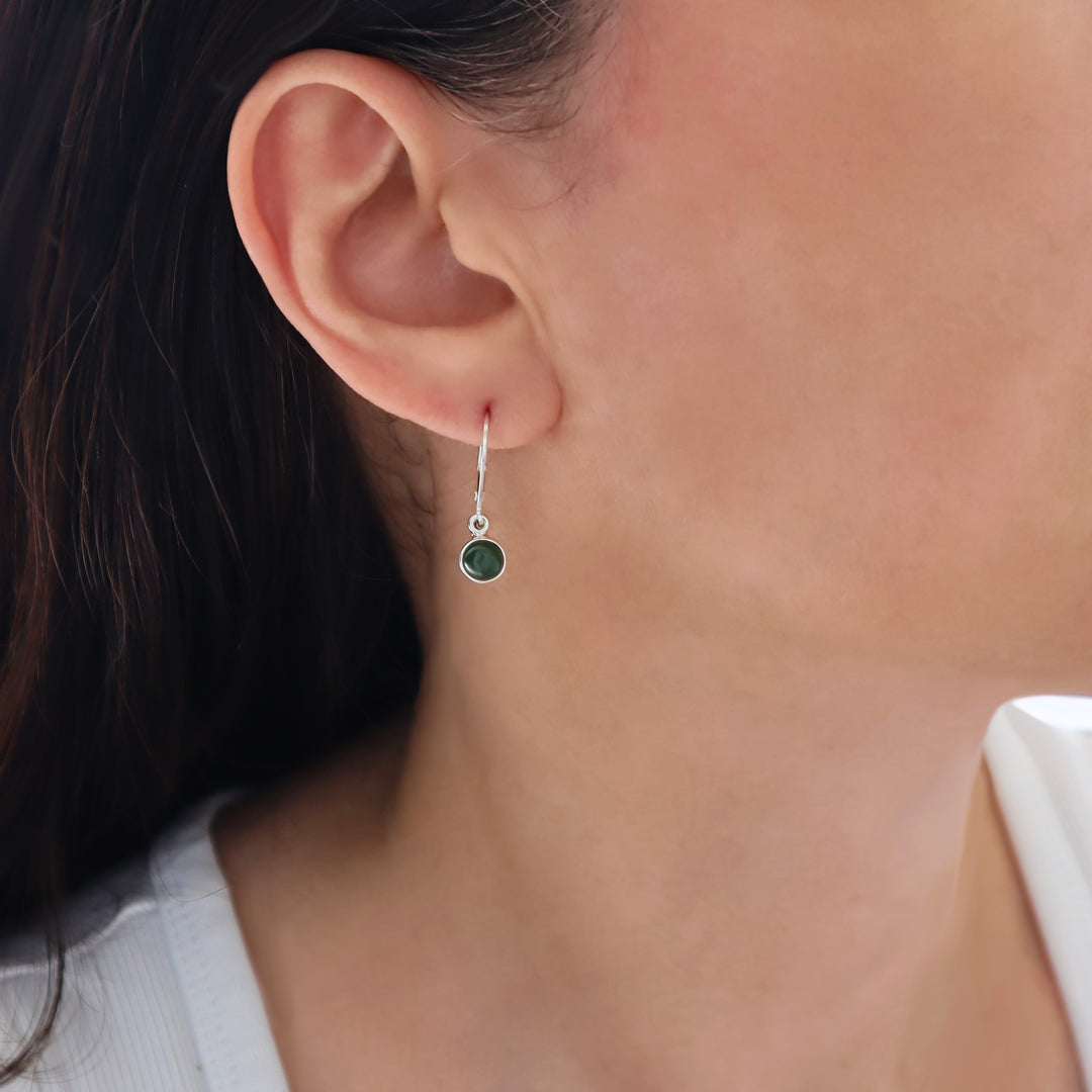 A close-up of a woman's ear wearing a delicate 925 silver dangle leverback earring with a small olive green jade stone.