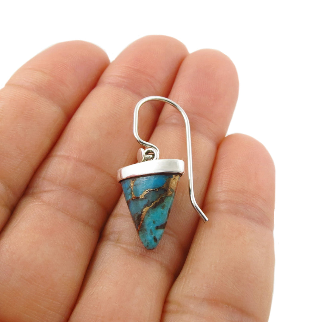A Taxco 925 silver drop earring with a triangular turquoise stone, held in a female hand against a white background.