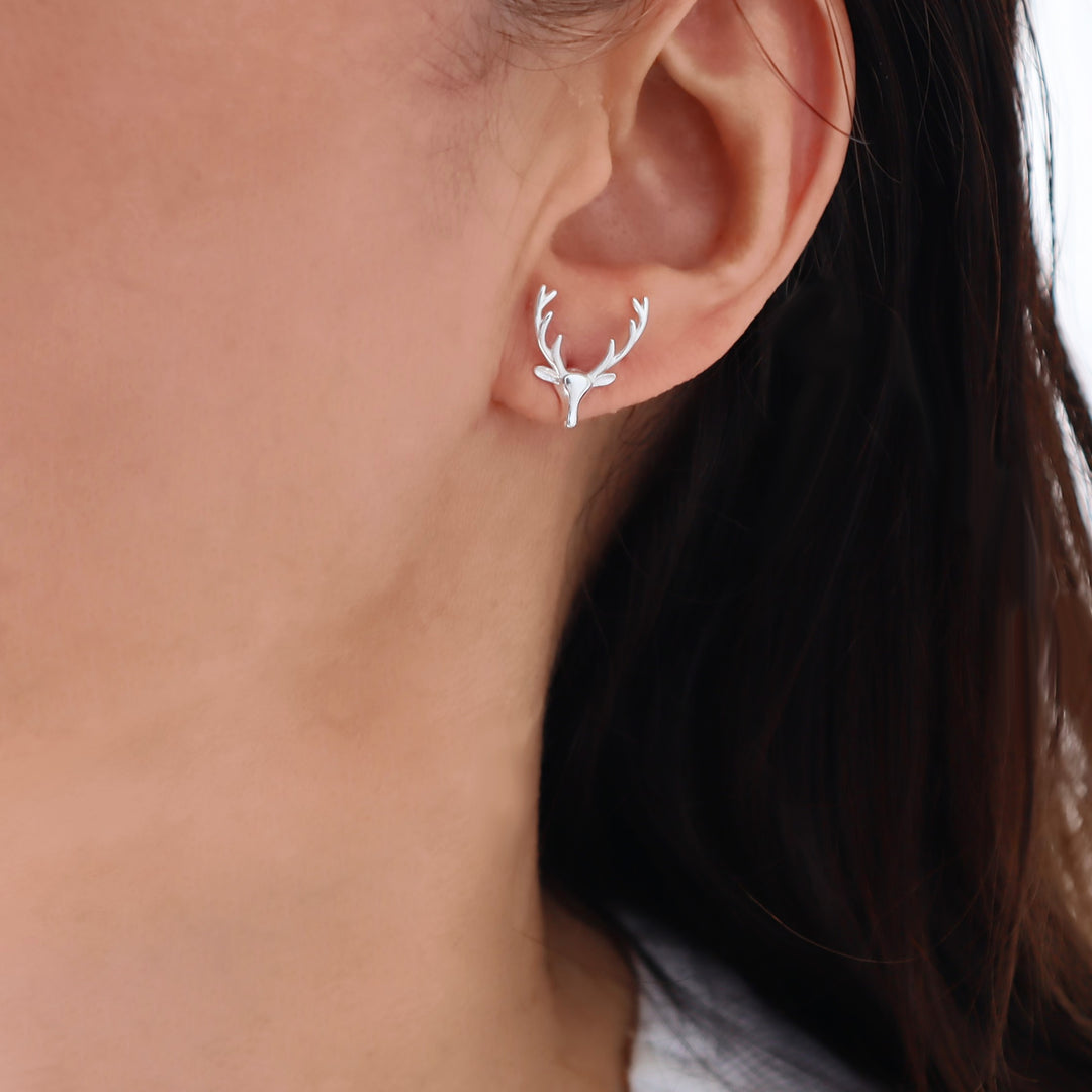 A close-up of a woman's ear wearing a large 925 sterling silver deer stag head and antlers stud earring.