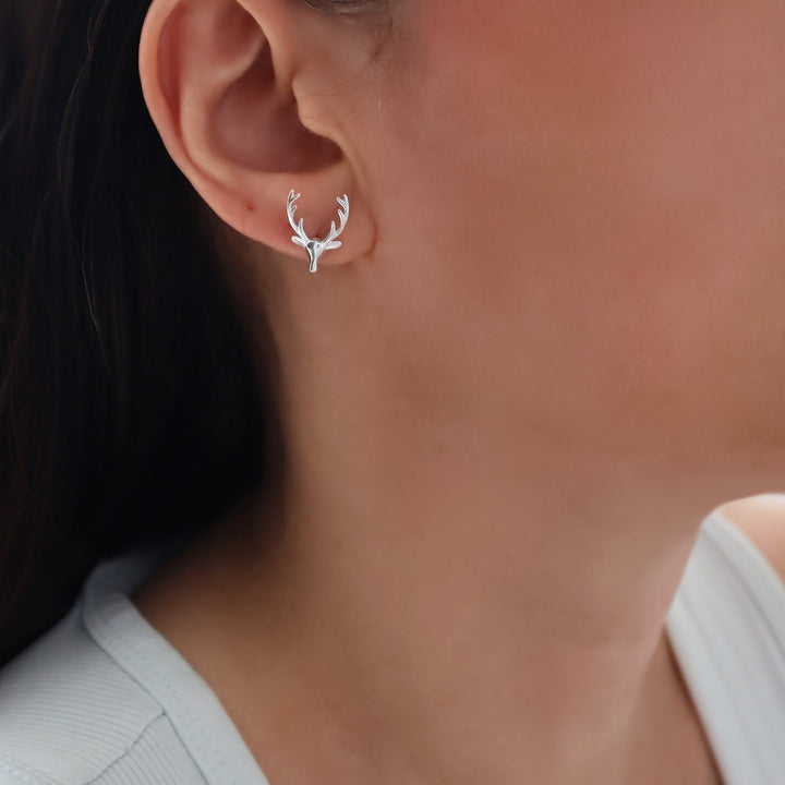 A close-up of a woman's ear wearing a large 925 sterling silver deer stag head and antlers stud earring.