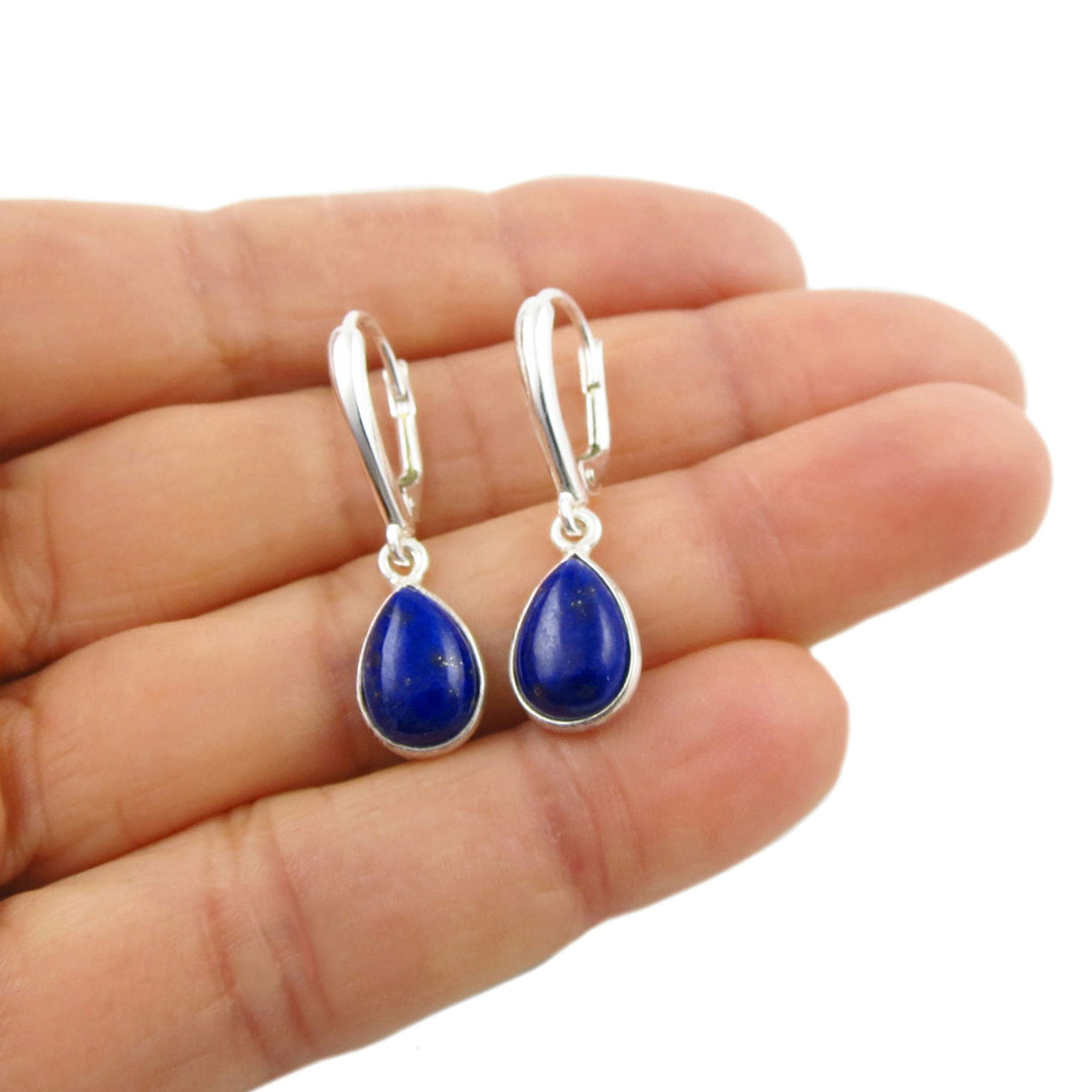 Long 925 sterling silver lapis lazuli gemstone dangling drop earrings held in a woman's hand on a white background. 