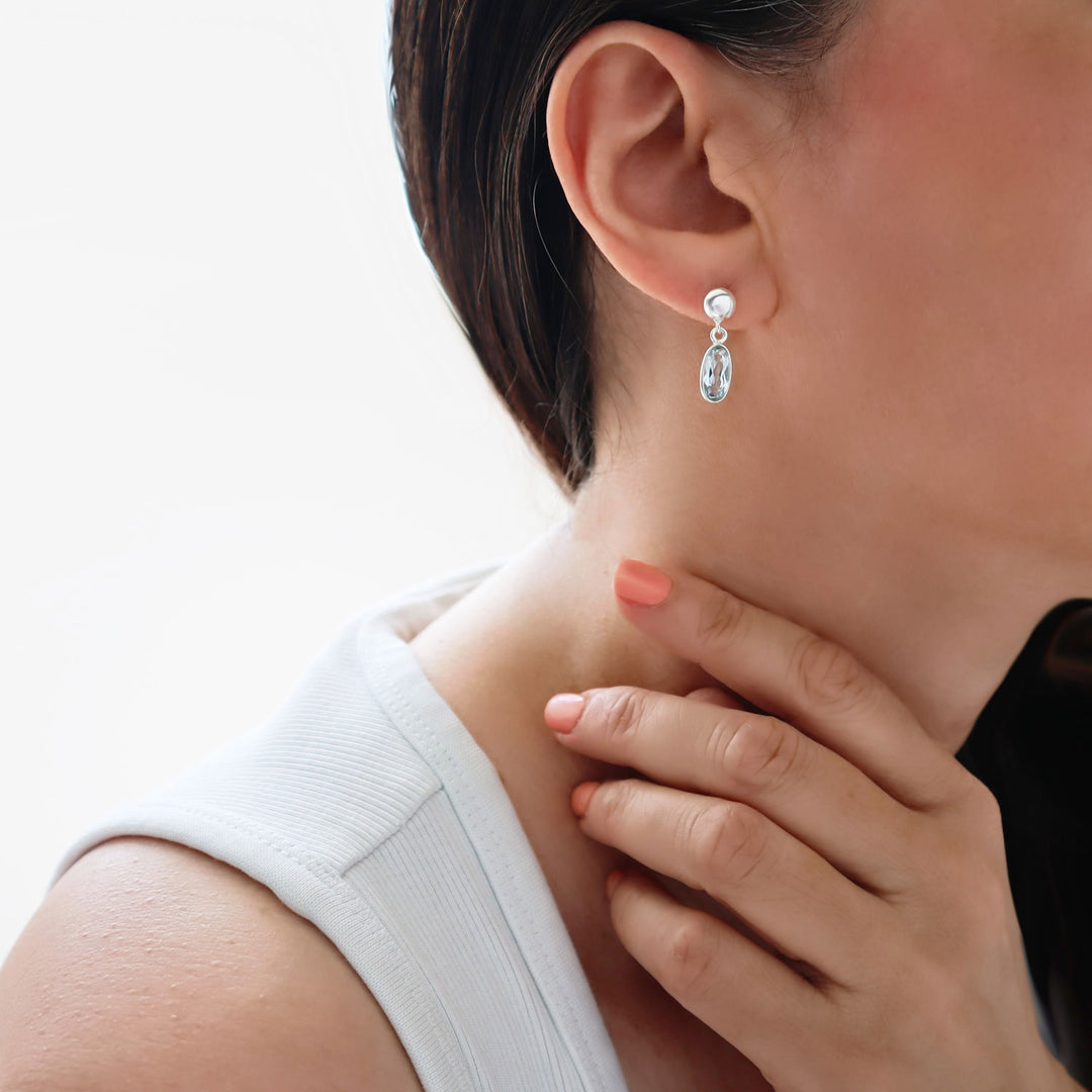 Long dangling blue topaz gemstone and 925 sterling silver earrings worn by a woman with dark hair and a white top