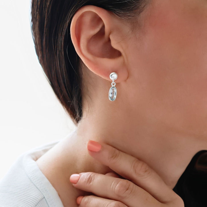 Faceted blue topaz and 925 sterling silver dangling drop earrings worn by a woman with dark hair