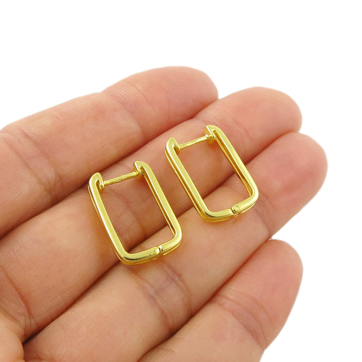 A pair of small 9ct yellow gold vermeil huggie hoop earrings held in a person's hand against a plain white background.