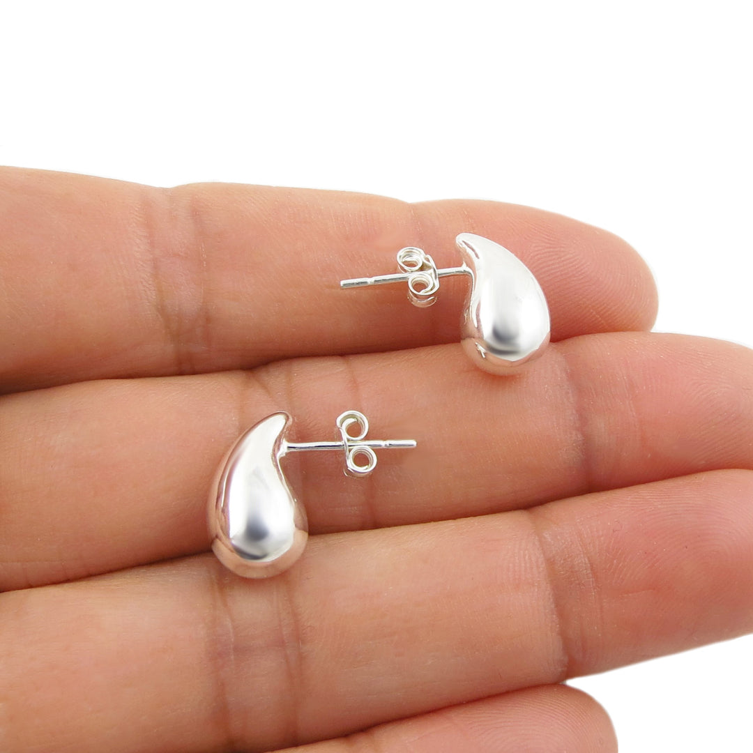 A pair of polished silver teardrop-shaped stud earrings displayed on a woman's fingers against a white background.