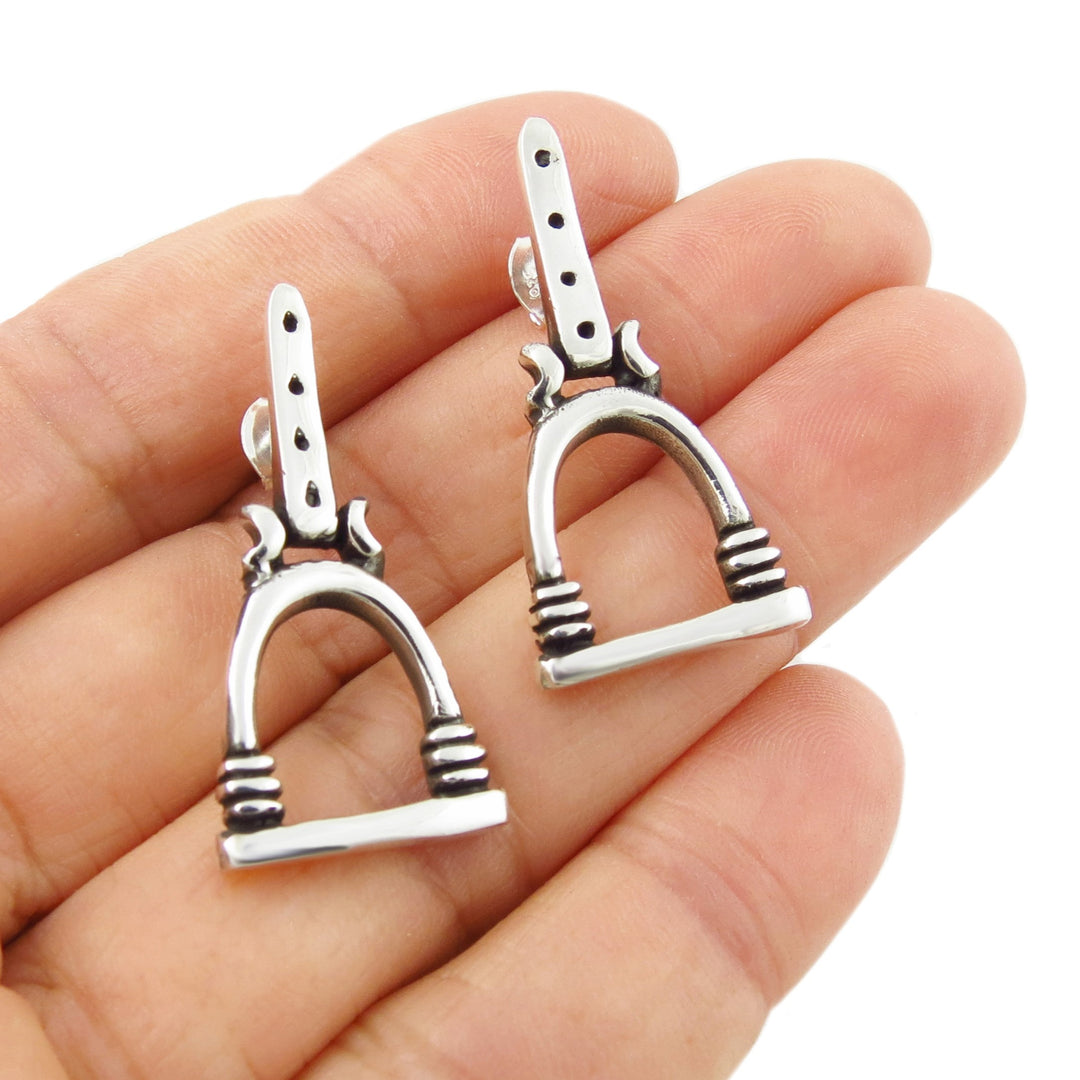 A pair of 925 sterling silver equestrian horse stirrup drop earrings held on a person's palm against a white background.