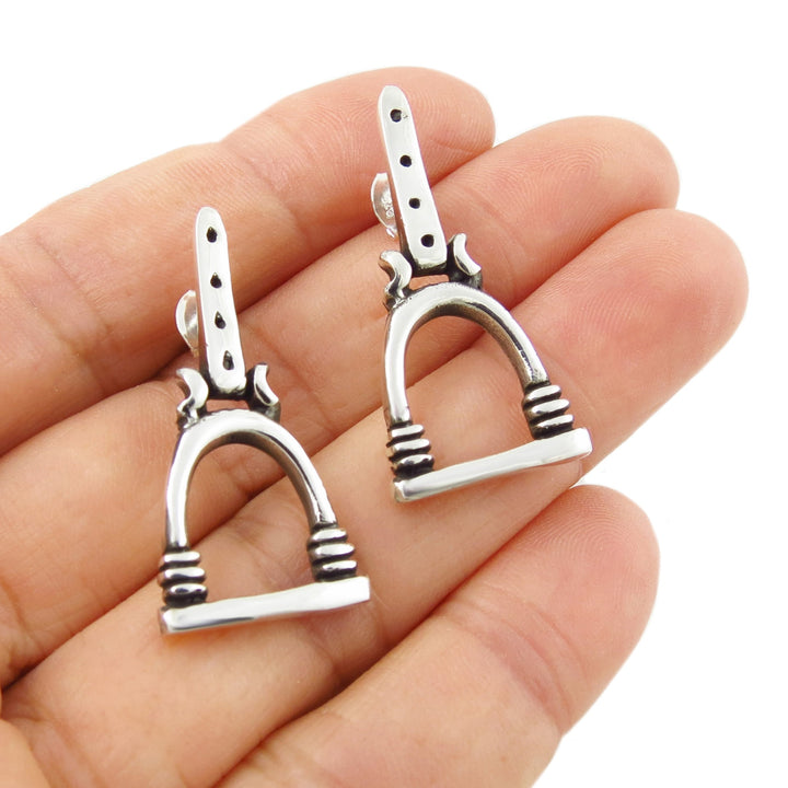 A pair of 925 sterling silver equestrian horse stirrup drop earrings held on a person's palm against a white background.