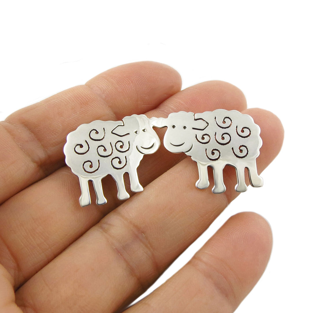 Sterling 925 silver sheep shaped country life design earrings held between fingers on a white background