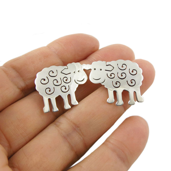 Sterling 925 silver sheep shaped country life design earrings held between fingers on a white background