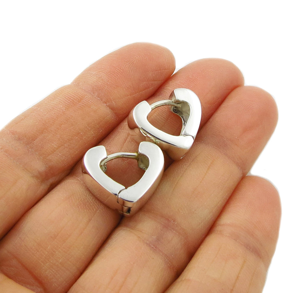A pair of polished 925 silver heart shaped huggie hoop earrings resting on a person's palm to show scale, against a clean white background.