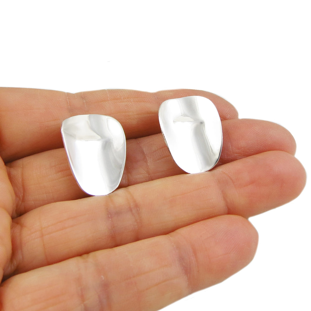 A pair of oval silver earrings held between fingers on a white background