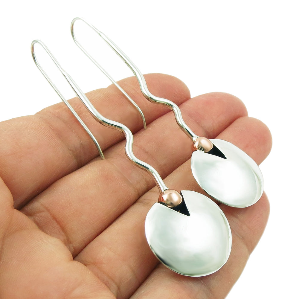 A pair of sterling 925 silver drop earrings with wavy stems, small mixed metal copper beads, and spoon-shaped silver discs, held in a woman's hand against a white background.