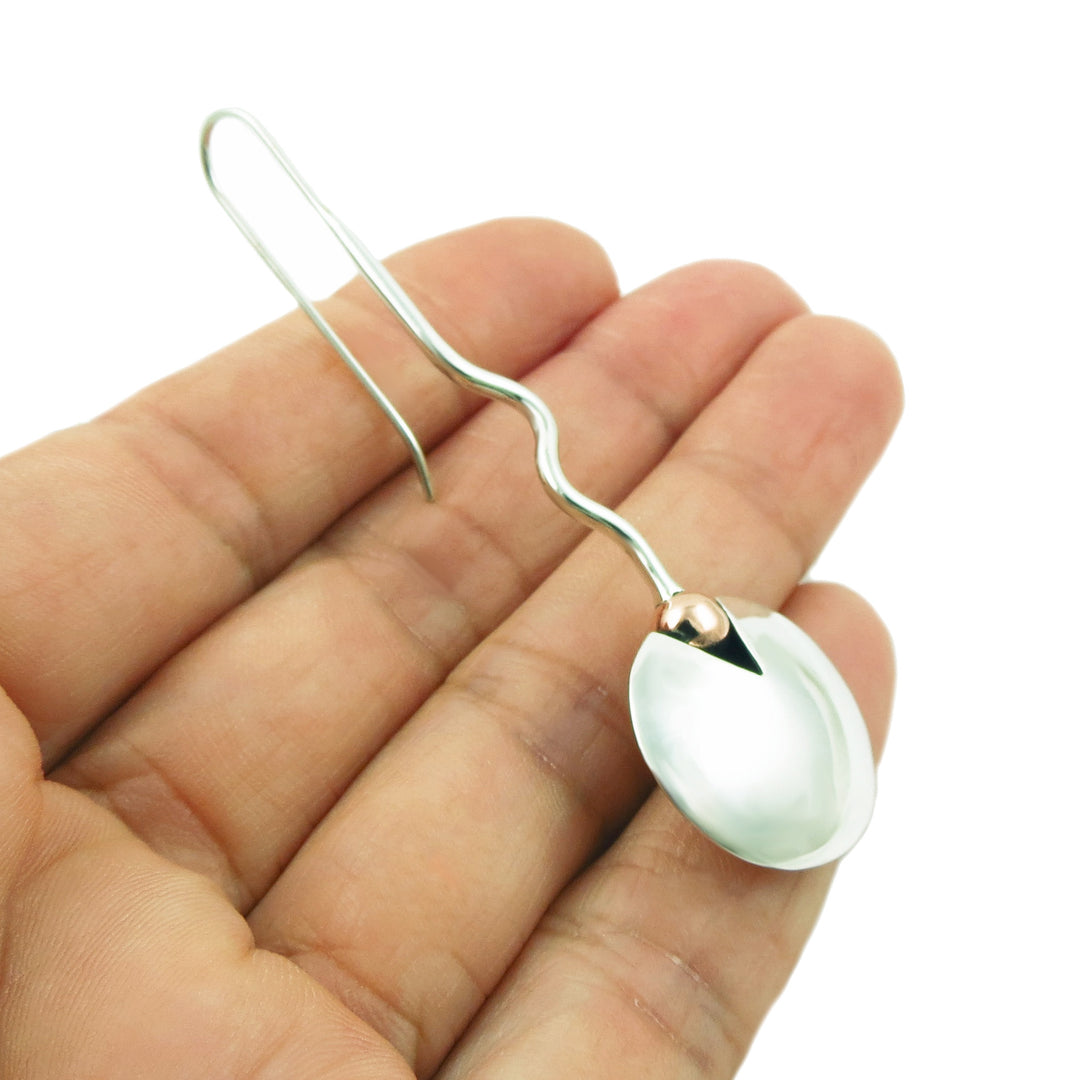 A mixed metal Mexican 925 silver wavy wire earring with a large circle disc with copper accents, held in a person's hand against a plain white background.