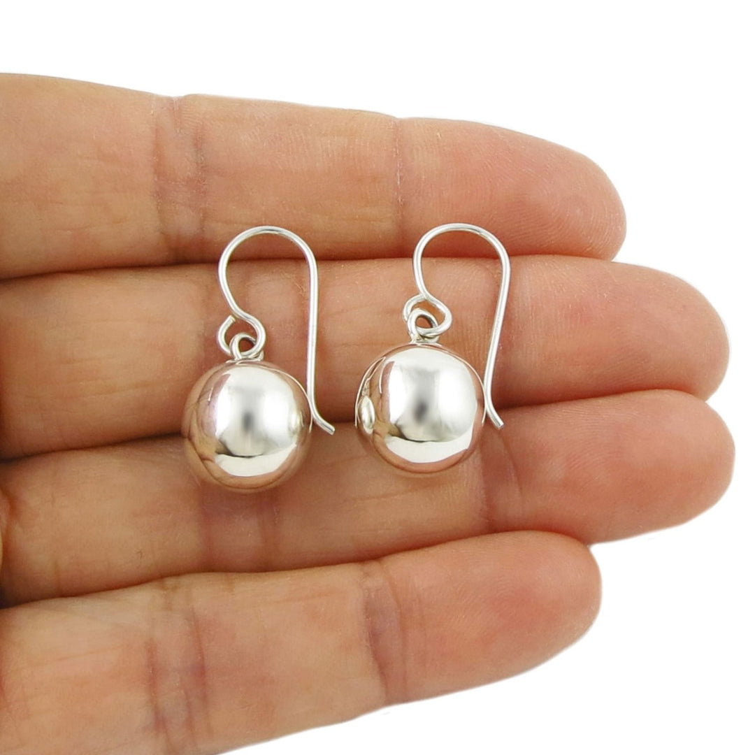 925 Silver ball bead earrings held in a woman's hand on a white background
