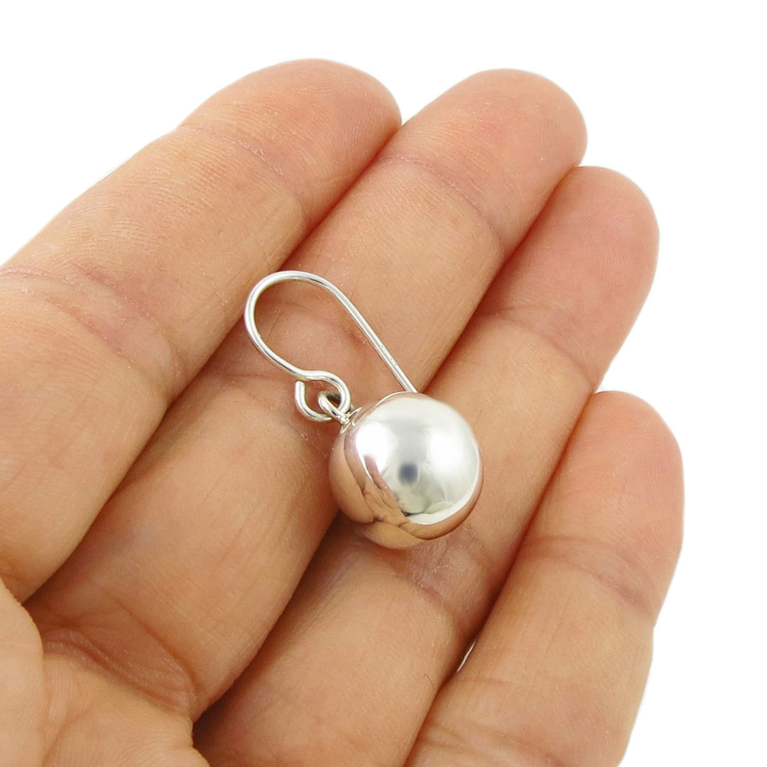 925 sterling silver dangling ball earring held between a woman's fingers on a white background