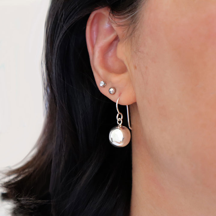 Close-up of a woman's ear wearing a ssterling 925 silver earring stack with studs and drops on a plain background